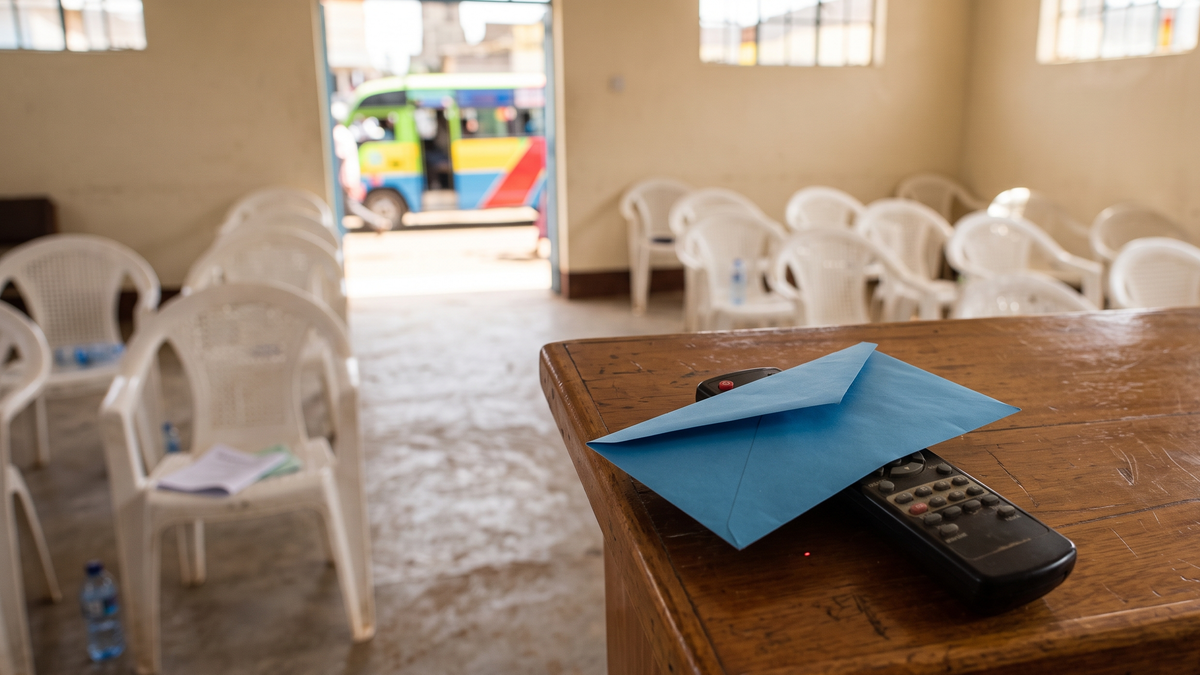 A blue offering envelope covering a projector remote in an empty Nairobi church hall.
